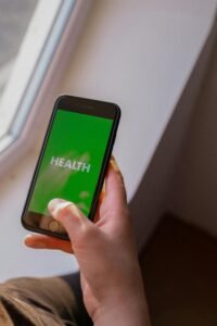 Close-up of a hand holding a smartphone displaying the word 'Health' on a green screen.